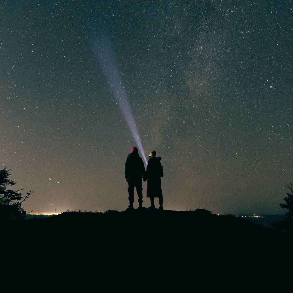 a couple holding hands infront of the night sky.